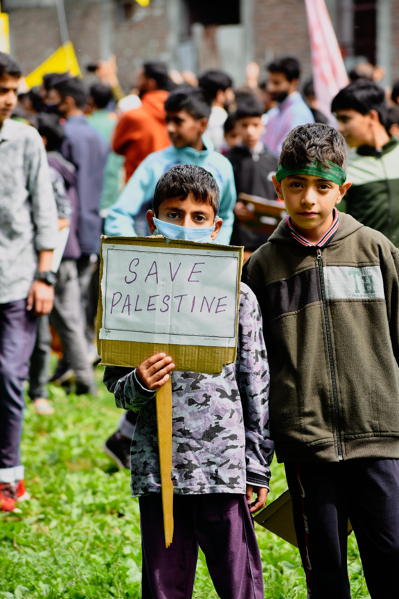 A boy holds a handwritten sign that says “Save Palestine.”