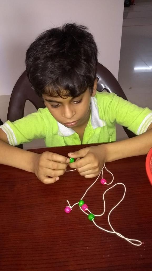 Child playing with beads and thread, putting in the beads into the thread.
