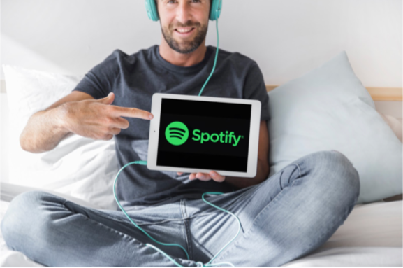 A young man holding a tablet, listening to music on the spotify app.