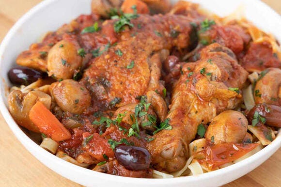 Chicken Cacciatore over pasta in a white bowl.