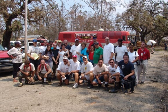 A group of volunteers including Firehouse Subs co-founders, Chris Sorensen and Robin Sorensen, pose for a photo in front of Fire-ONE (the Firehouse Subs bus) after Hurricane Katrina.