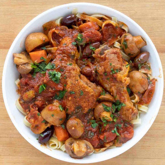 Chicken Cacciatore over pasta in a white bowl.