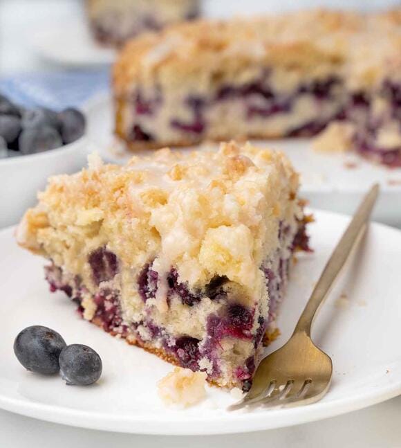 Slice of blueberry coffee cake on a white plate with a fork.