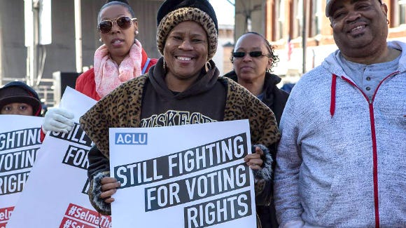 A Black woman at a march holding a sign that reads: “ACLU: STILL FIGHTING FOR VOTING RIGHTS”