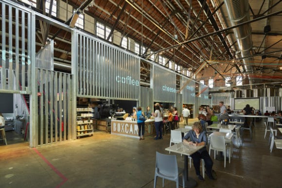 People sitting, eating, and shopping at a coffee shop in a large warehouse.