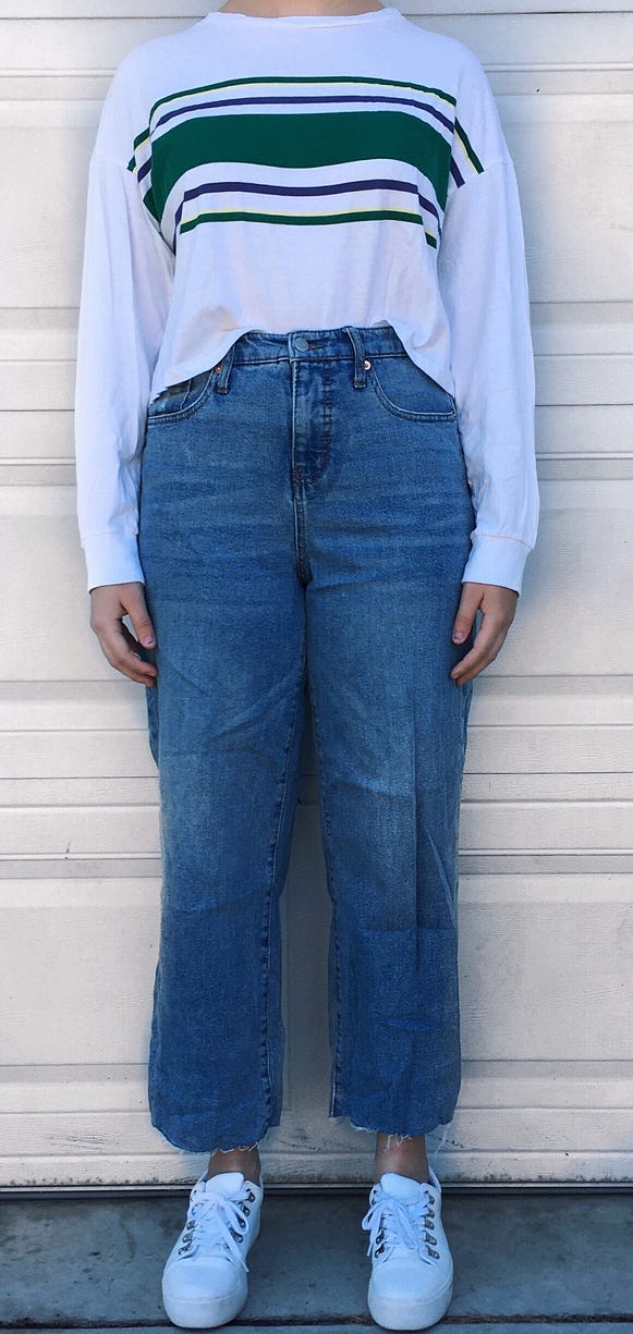 High-waisted cutoff jeans worn with a white long sleeve shirt that has green and purple stripes across the front.