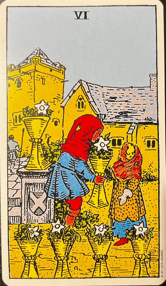 The VI of cups from the Rider-Waite-Smith Tarot Deck — Two children in a village garden. One is holding a cup with a single white flower and smelling the flower.
