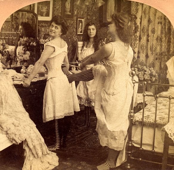 The image is set in a dressing room depicting ladies assisting a woman in putting on a corset.