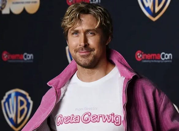 Ryan Gosling in a white shirt that reads “From Director Greta Gerwig” in the iconic Barbie font. Under a pink jacket to boot.