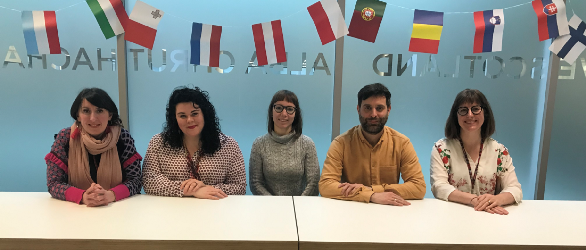 Photo of Team Lit sitting in a row at a white table with colourful flag bunting hanging on the wall above our heads