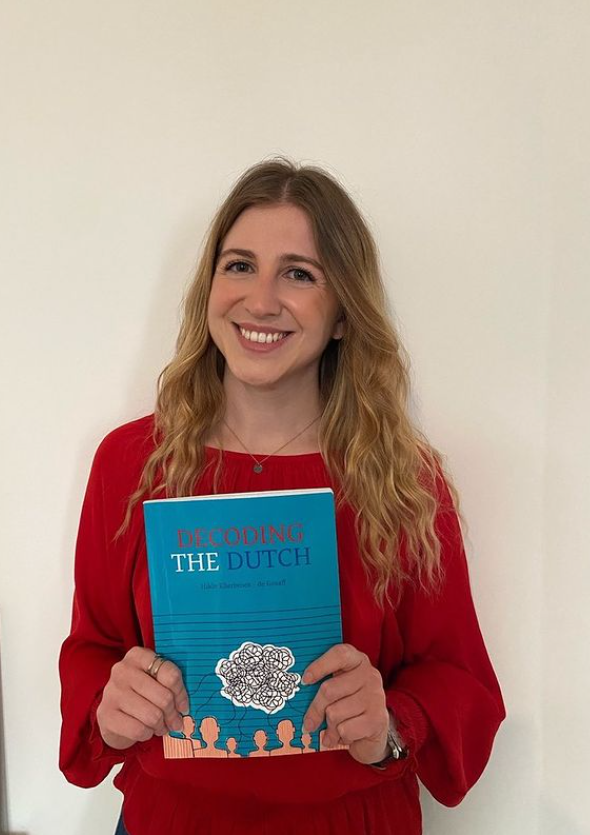 Woman poses against a white wall while holding a book about Dutch culture.