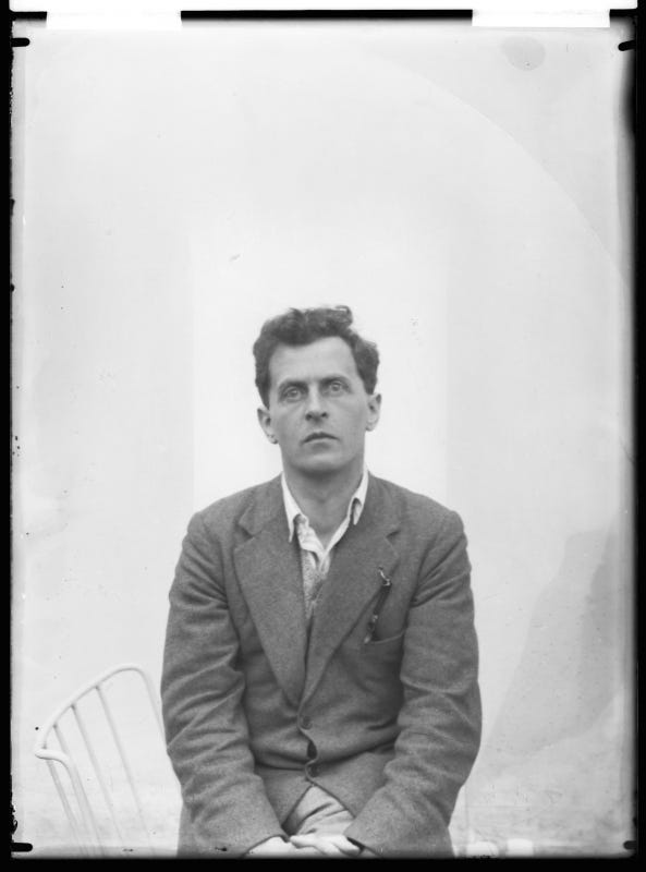 A black and white portrait of Ludwig Wittgenstein (1889–1951), Austrian philosopher, logician, and mathematician. He appears pensive, gazing off to his right with intense focus. Wittgenstein has dark hair, is dressed in a buttoned-up shirt and a tweed jacket with a pocket square, and sits with his hands folded in his lap. The background is overexposed, giving his figure a slight halo effect. A white chair is partially visible to his left.