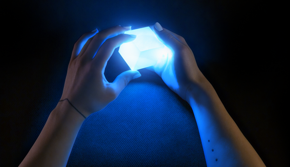 Two real human hands holding a glowing virtual cube seen through a Microsoft Hololens to demonstrate their new immersive interactions concept