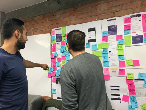 Two members of the BT Design team look at a board of Post-It notes about a research project.