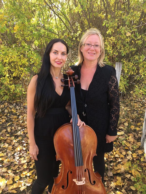 2 women standing outside in formalwear, one holds a cello