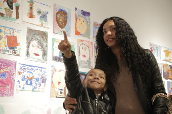 A wall full of artwork and a face full of wonder. A child pointing his family member to his piece.