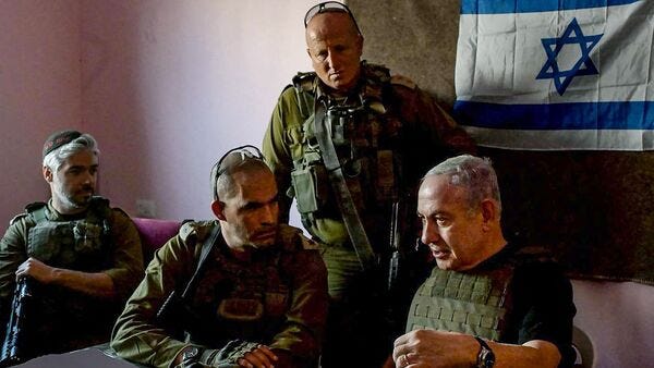 A picture of Benjamin Netanyahu in a room with some Israeli military personnel, with the Israeli flag hung on a wall in the background.