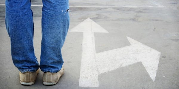 Arrow on pavement pointing straight ahead, with another pointing to the side. Feet standing at that point—indicating making a choice.