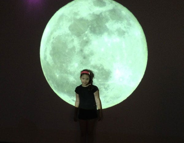 A little girl with a huge moon image at the background