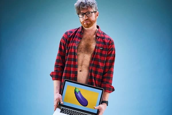 Man with an unbuttoned shirt holding a laptop with an eggplant emoji picture in front of his groin area.
