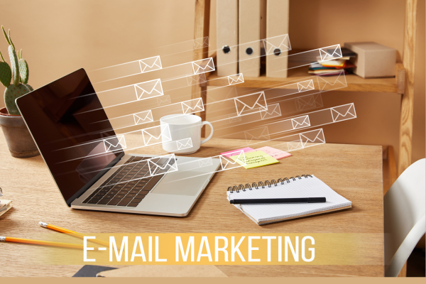 laptop with email icons and ‘email marketing’ lettering on wooden table at home