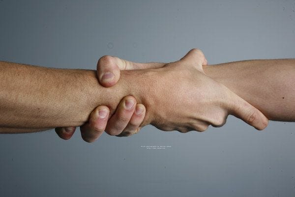 The hands of two people clasped at the wrist.