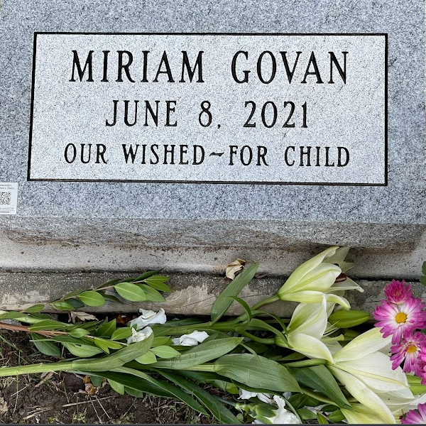The image of a child’s tombstone. Flowers below it.