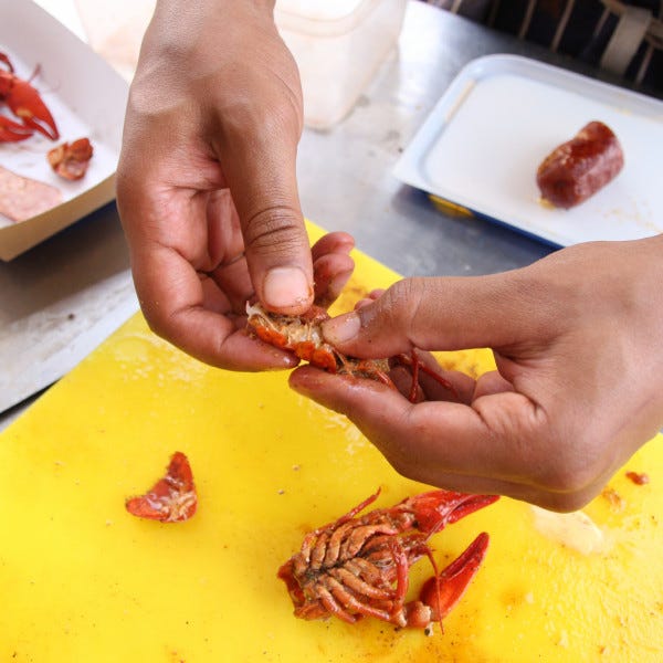 person removing tail from cooked crayfish