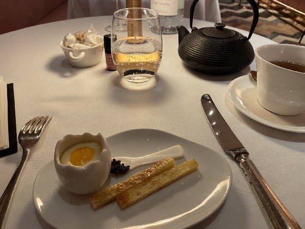 a Plate with a shelf shaped egg holder filled with what looks like a runny egg and two thing toast strips next to it