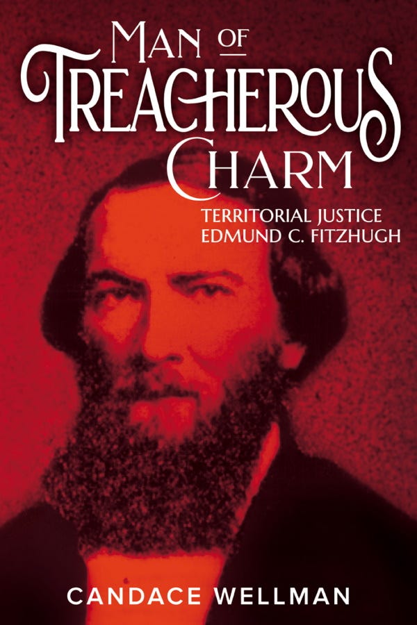 A book cover is shown with a reproduction of an old photograph with a red filter. The portrait photo is of a man with medium length hair and a bushy mustache and beard. He appears to be wearing a shirt and jacket and looks directly into the camera. The title of the book appears at top in white text and reads, “Man of Treacherous Charm: Territorial Justice Edmund C. Fitzhugh.” The author’s name is at bottom in white text and reads, “Candace Wellman.”