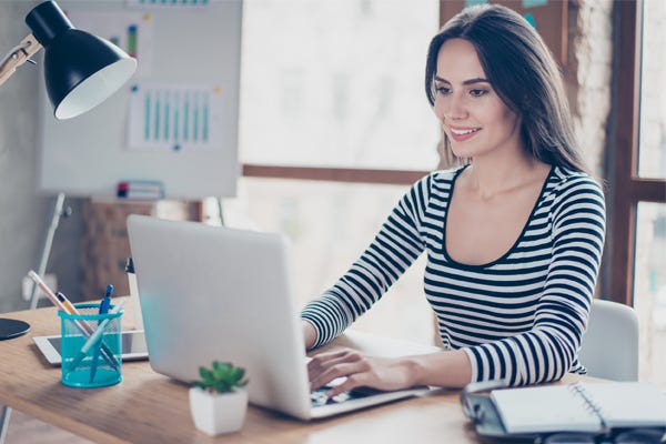 Freelancer/Consultant smiling woman typing on laptop in a bright modern office.