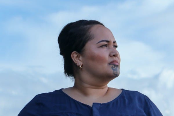 A Māori woman with a moko kauae looks off into the distance. She looks like she is thinking deeply.