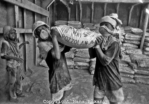 Two children carrying a bag of cement in a factory