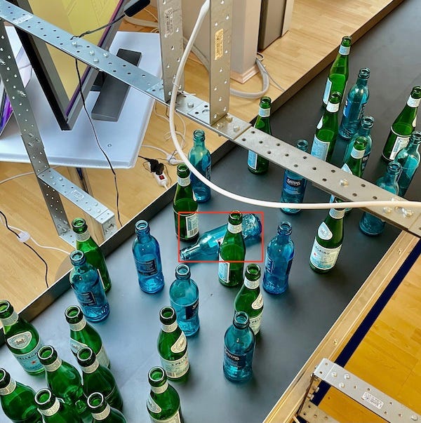Image showing standing bottles and a fallen bottle on a conveyor belt. The fallen bottle is labeled with a bounding boxes assigned by our fine-tuned YOLOv7.