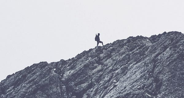 Silhouette of a mountaineer standing on an ascending ridge; photo all black & white.