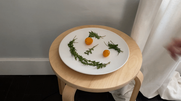 Person removing arugula and tomatoes in the shape of a happy face on a plate and replacing it with a sad face of red m&ms.