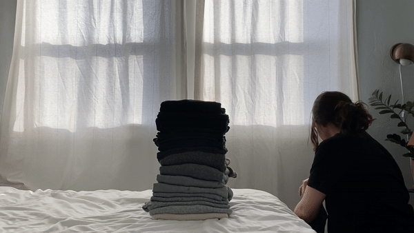 Person adding folded clothes to a tall stack organized from white to black.