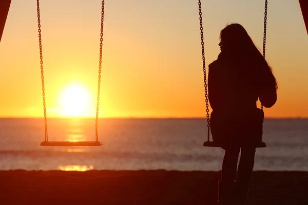 A girl sitting alone on a swing at the beach, gazing at the empty seat beside her, feeling lonely.