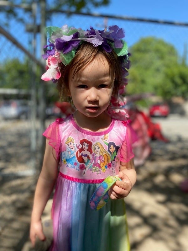 A little girl wearing a rainbow-colored dress with a flower crown on her head.