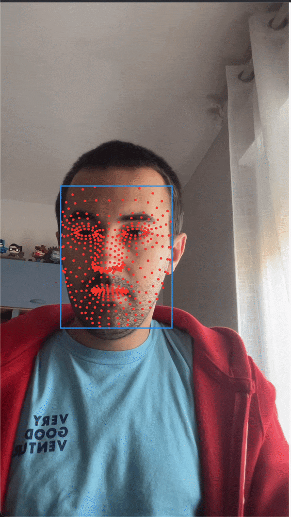 A man wearing a light blue shirt and red hoodie is moving his face around the screen. There is a blue box around his face and red dots mapping onto his face, with a high concentration of dots around his eyes and mouth. As he moves his face, red dots move along with his facial features.