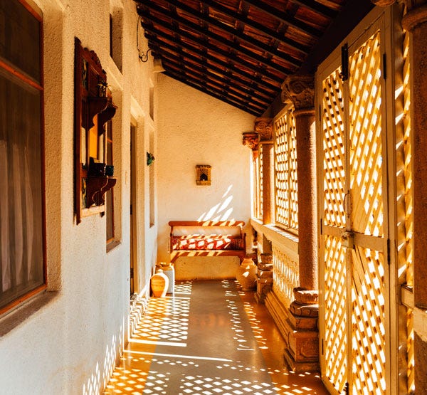 A sun-dappled breezeway with wooden benches at the Bhuj House.