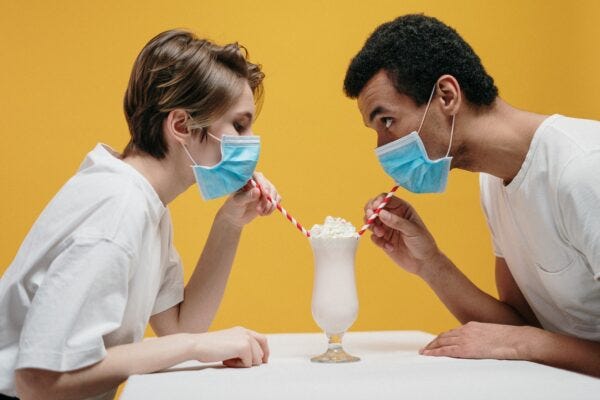 A man and a woman wearing surgical face masks share a milkshake