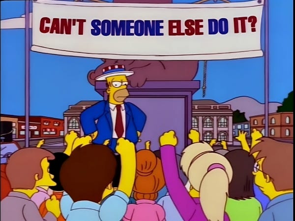 A still from the Simpsons with Homer standing in front of a crowd in front of a sign that says “Can’t someone else do it?”