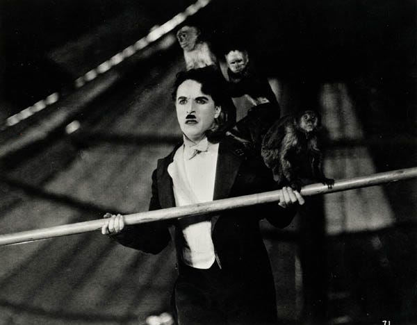 Charles Chaplin in The Circus, 1928. The scene shows a bewildered Charles Chaplin precariously balancing on a tightrope with three monkeys on his back.