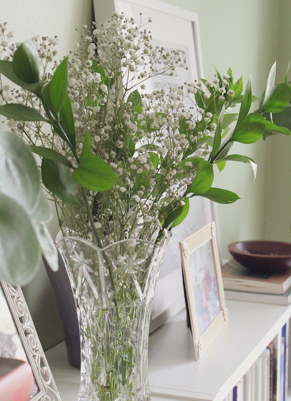 A glass vase filled with greenery and baby’s breath on a bookshelf