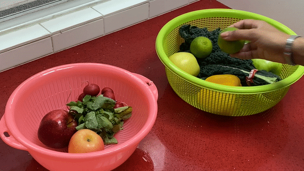 Person sorting green and yellow, pink and red fruits and vegetables into two different bowls.