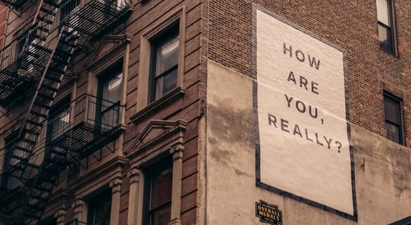 Quote painted on the side of a building reading: “How are you, really?”