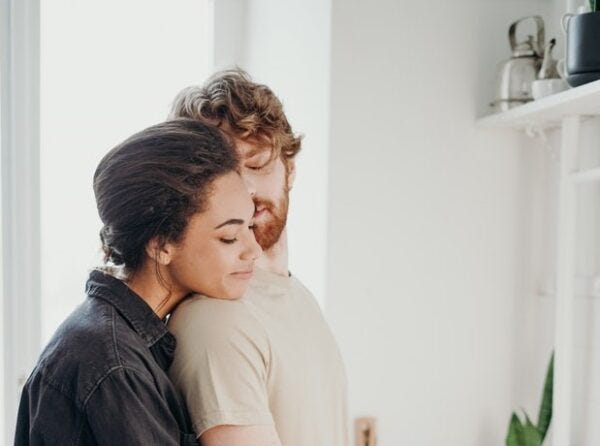 a woman hugs a man from behind while he looks back at her