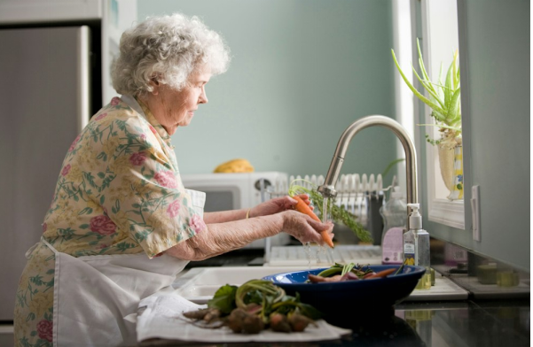 An elderly woman washing carrots in a kitchen sink.