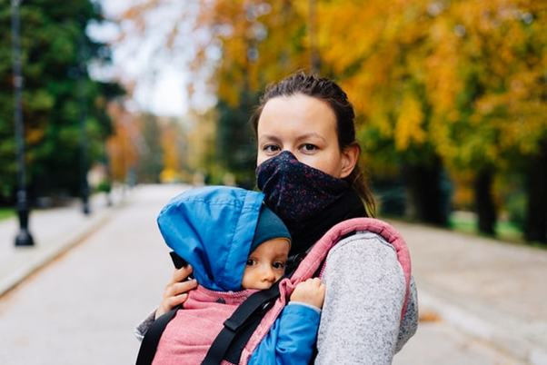 Woman wearing mask holding baby in carrier